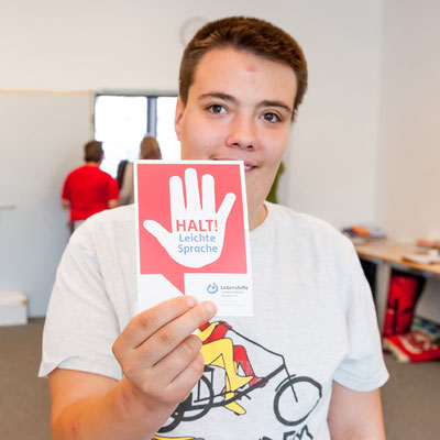 Eine Person hä#lt ein Schild hoch "Halt - leicht Sprache".