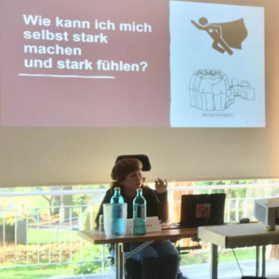 Eine Person hält einen Vortrag, vor ihr auf dem Tisch steht ein Laptop.